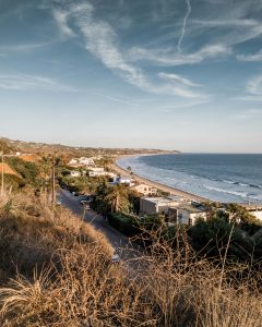 Aerial view of Malibu coastline with ocean, beach, and residential area under a clear sky.