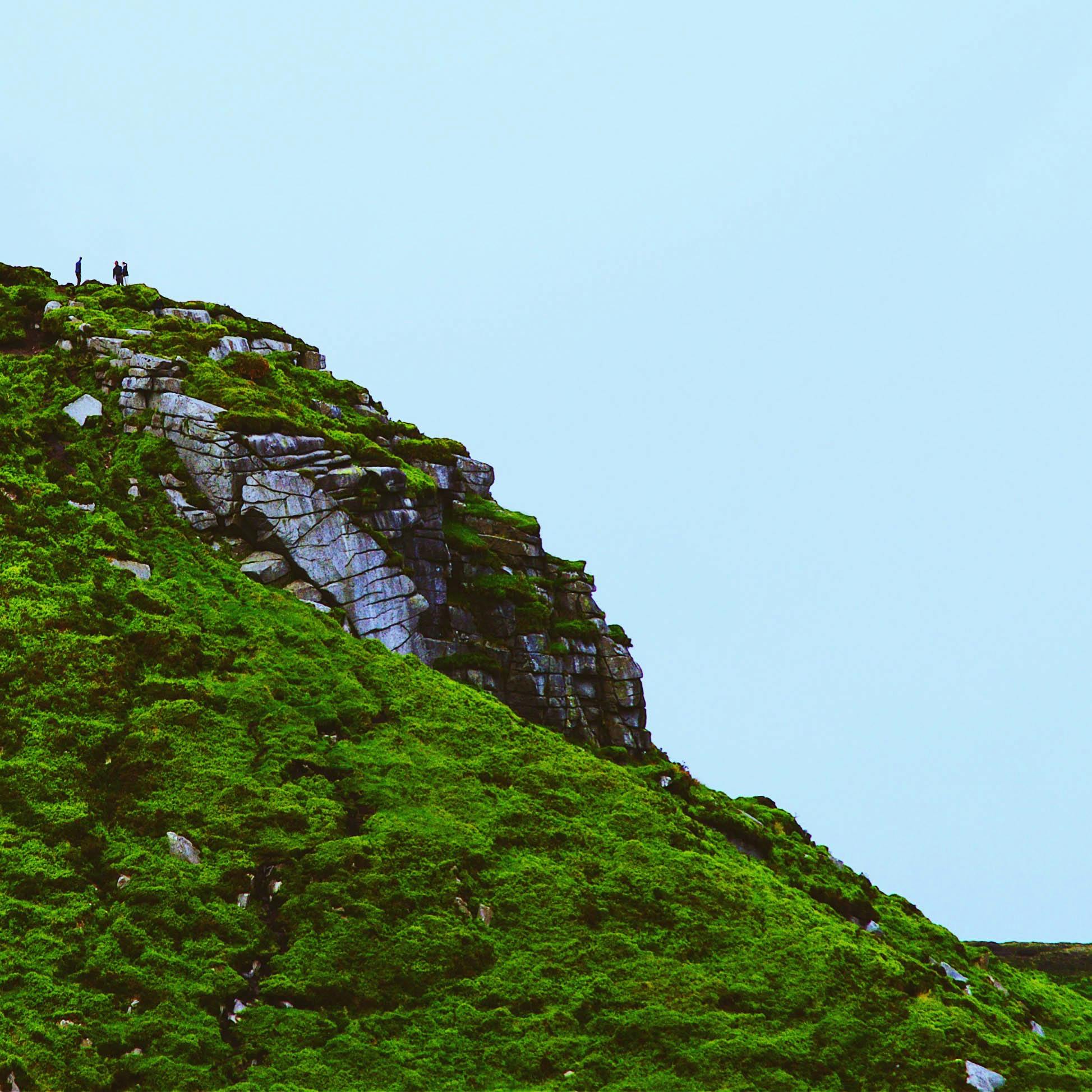 Hikers explore a lush green mountain slope in County Wicklow, Ireland under a clear blue sky.